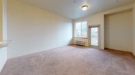 This single-floor residence offers a practical and comfortable layout designed for everyday living. The living area is generously sized, finished with warm neutral carpet, and filled with natural light through a large window and a glass door that opens to a private balcony, providing pleasant outdoor views. A wall-mounted PTAC unit ensures year-round climate control, while a flush-mount ceiling light keeps the space well-lit.

The galley-style kitchen is efficiently arranged with warm oak cabinetry lining both sides, offering ample upper and lower storage. Light-toned countertops provide a clean work surface, and the kitchen is equipped with a full suite of white appliances, including a range, dishwasher, refrigerator, and built-in microwave. Light tile flooring completes the practical and easy-to-maintain space. A passthrough view from the kitchen connects to the hallway, where a stacked in-unit washer and dryer are conveniently located.

The bedroom features plush carpeting, a ceiling fan with integrated lighting, a natural light window, and a built-in closet with sliding doors, offering generous storage. The bathroom is finished with tile flooring, a full bathtub with shower, and accessibility-friendly grab bars, complemented by a vanity with warm wood cabinetry. Throughout, the residence maintains a clean, neutral palette that creates a calm and welcoming ambiance.