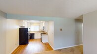 This single-floor residence offers a practical and comfortable layout designed for efficient everyday living. The open-concept living area features plush wall-to-wall carpeting and soft blue-gray walls, creating a calm and welcoming atmosphere. A large window in the living room allows natural light to fill the space while providing views of the surrounding greenery. A wall-unit air conditioner and baseboard heating ensure year-round comfort.

The kitchen opens seamlessly to the living area through a wide pass-through opening and is finished with crisp white cabinetry, granite-style countertops, and hardwood-style flooring. It is equipped with a full suite of appliances including a black refrigerator, gas range, built-in microwave, and dishwasher. A double stainless steel sink sits beneath a window with vertical blinds, adding both functionality and natural light to the workspace.

The bedroom is generously sized with carpeted flooring and direct access to a private bathroom featuring a walk-in shower with chrome fixtures, a vanity with granite countertops, and tile flooring. A second full bathroom includes a tub-shower combination with sliding glass doors, a single vanity, and a lighted mirror. The textured ceilings are consistent throughout, contributing to the cohesive character of the space.