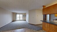Located in Champlin, Minnesota, this two-bedroom, one-bathroom residence offers a practical and well-organized single-floor layout. The open living room is carpeted and features a sliding glass door leading to a private balcony with outdoor views, along with a wall-mounted air conditioning unit and baseboard heating for year-round comfort. A textured ceiling adds character to the space. The kitchen is designed as a galley-style layout, featuring warm oak cabinetry, dark laminate countertops, tile flooring, and white appliances including a range, dishwasher, and refrigerator. A breakfast bar with an overhanging oak counter connects the kitchen to the living area, creating a convenient pass-through space. Both bedrooms are carpeted and equipped with baseboard heating. The primary bedroom is comfortably sized and includes a window with outdoor views and a dedicated closet. The second bedroom is also carpeted with its own window. The full bathroom includes a wide oak vanity with ample counter space, a large mirror, tile flooring, and a shower/tub combination. Two closets throughout the unit provide practical storage solutions. Neutral wall tones and consistent finishes create a cohesive and functional living environment throughout.