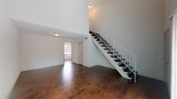 This two-story space is defined by its impressive vertical scale, with soaring ceilings in the main living area that create an open, airy atmosphere. Rich, dark hardwood flooring flows consistently throughout both levels, providing warmth and visual continuity across the space.

The main living area is generously proportioned, anchored by a dramatic open staircase with dark treads and a sleek white metal railing system that serves as a architectural focal point. Natural light filters in through windows and a sliding glass door, enhancing the bright, clean aesthetic established by the white walls throughout.

The kitchen is well-appointed with white cabinetry, granite countertops, a tile backsplash, stainless steel appliances including an electric range, and a double basin sink — offering both functionality and a polished finish.

One of the bedrooms includes a walk-in closet and a stacked washer and dryer unit, providing convenient in-unit laundry. Additional bedrooms are well-sized with clean lines and ample floor space. The bathroom features tile flooring, a full tub-shower combination with floor-to-ceiling tile surround, a toilet, and a vanity with granite countertops, maintaining the consistent, contemporary finishes found throughout the space.