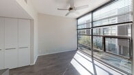 Located at Alta in San Diego's vibrant Middletown neighborhood, Unit #244 at 2015 Hancock Street is a thoughtfully designed two-story residence that blends modern aesthetics with functional living. The layout spans two levels connected by an interior staircase, offering a clear separation between living and private spaces.

The main living area features wide-plank hardwood-style flooring and expansive floor-to-ceiling windows framed in dark metal, flooding the room with natural light and providing views of the surrounding urban greenery. A ceiling fan adds both style and practicality to this airy space.

The kitchen is outfitted with sleek white cabinetry, stainless steel countertops, a glass tile backsplash, and stainless steel appliances including a built-in microwave, electric cooktop, and oven — creating a clean, contemporary workspace.

The bedroom is carpeted for comfort and features the same generous floor-to-ceiling window treatment, continuing the home's commitment to natural light and outdoor connectivity.

The bathrooms are finished with distinctive green mosaic tile accents paired with crisp white surfaces. One bathroom includes a soaking tub with a showerhead, while the other offers a glass-enclosed walk-in shower, a wall-mounted toilet, and a pedestal vanity — both delivering a polished, spa-inspired feel throughout.