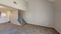 Located in Wichita, KS, this two-story, 2-bedroom, 1-bathroom home offers a practical and comfortable layout spread across two floors. The main level features a kitchen equipped with warm honey-oak cabinetry, an electric range, a refrigerator, a dishwasher, and a decorative tin-style backsplash. Hardwood-style flooring runs through the kitchen and entry hallway, adding a clean, cohesive look to the main level. The spacious living room is anchored by soaring vaulted ceilings and a staircase with a metal railing leading to the upper floor, creating an open and airy atmosphere. The living area is carpeted and benefits from generous vertical space. Both bedrooms are carpeted and feature neutral tones, with the primary bedroom boasting vaulted ceilings, high clerestory windows for added natural light, and dual closets including a mirrored sliding-door closet. The second bedroom includes a sliding glass door with vertical blinds. The bathroom features a full tub and shower combo with a clean white surround and built-in shelving niche. Textured ceilings are present throughout, and the overall color palette of warm neutrals gives the home a calm, welcoming ambiance.