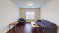 Located at 16 Kenneth Ave in Shippensburg, PA, this single-floor unit offers a practical and well-organized layout designed for comfortable everyday living. The interior is finished with neutral, warm-toned walls throughout, creating a clean and consistent aesthetic across all rooms.

The living area features rich, dark hardwood-style flooring that adds warmth and contrast to the light walls, with a window allowing natural light to fill the space. The kitchen is outfitted with medium-toned oak cabinetry, dark countertops, light tile flooring, and white appliances including a refrigerator, electric range, microwave, and a sink with ample counter space on either side.

The bedrooms are carpeted for comfort and each includes a window with blinds that provides natural light. The rooms are modestly sized and well-suited for use as individual sleeping quarters or study spaces.

The bathroom features a vanity with oak cabinetry, a white countertop, an oval framed mirror, a window for natural light, and a dedicated walk-in shower stall with clean white surround. A dedicated laundry area accommodates a full-sized washer and dryer side by side, with overhead wire shelving for added storage. A hallway connects the rooms and includes an electrical panel access point.