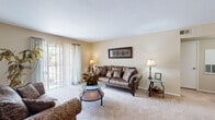This efficiently designed single-floor residence offers a thoughtful layout encompassing a living room, dining area, kitchen, one bedroom, and one bathroom. The inviting living room is bathed in natural light through a large sliding glass door fitted with sheer vertical blinds, providing outdoor views and a bright, airy ambiance. Neutral-toned carpet and warm beige walls create a cohesive and welcoming atmosphere throughout the main living area. The adjacent dining space accommodates a cozy dining set and is accented by framed wall art, adding a touch of character. The galley-style kitchen features dark cabinetry with granite-look countertops, white subway tile backsplash, hardwood-style flooring, and includes a full suite of appliances — offering a practical and stylish cooking space. The bedroom is a comfortable retreat, highlighted by a ceiling fan with light fixture, carpeted flooring, a window with outdoor views, and ample space for furnishings. The bathroom is well-appointed with dark wood cabinetry, a granite-look vanity countertop, a full tub-shower combination with white tile surround, and hardwood-style flooring, completing this functional and attractive home.