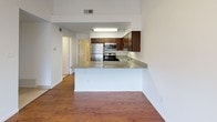 This single-floor residence offers a well-designed layout that balances comfort and functionality. The open-concept kitchen serves as a central highlight, featuring rich dark wood cabinetry, granite countertops, stainless steel appliances including a refrigerator, microwave, and range, and a peninsula that provides additional prep space and a natural divide between the kitchen and the main living area. Hardwood-style flooring runs throughout, lending warmth and continuity to the space.

The living area is anchored by a classic fireplace with a marble-style surround, creating a cozy focal point. Vaulted or elevated ceiling lines, visible in the overhead view, add a sense of openness and volume to the main living space. A dedicated bedroom features the same hardwood-style flooring, a ceiling fan with integrated lighting, and a textured ceiling, offering a comfortable and practical retreat.

The bathroom is clean and functional, with white tile walls accented by a decorative mosaic border strip in warm earth tones, a full soaking tub with an overhead shower, chrome fixtures, and granite countertop detailing. Throughout the space, neutral white walls provide a versatile backdrop that complements the warm wood tones and stone finishes, creating a cohesive and inviting atmosphere.