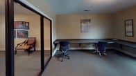 This single-floor space is designed to serve as a functional office and amenity area, offering several distinct zones suited for work and recreation. The primary office area features warm beige walls, carpeted flooring, and multiple ergonomic task chairs positioned around dark wood desks and a multi-drawer filing cabinet. A window with horizontal blinds allows natural light to filter into the room, complementing the overhead ventilation system integrated into the ceiling.

A glass-partitioned computer workstation room provides a semi-private workspace, equipped with a long built-in counter-height desk running along the wall and accompanied by task chairs. Decorative artwork adorns the walls, and the room benefits from visibility into the adjacent amenity space through full-height sliding glass doors with dark frames.

Beyond the glass partition lies a spacious game room distinguished by bold accent walls, recessed lighting, and a full-size pool table as a centerpiece. Additional seating and tables are arranged throughout, creating an inviting recreational atmosphere. The overall layout connects the professional workspace seamlessly with the leisure area, making this a versatile, multi-purpose facility.