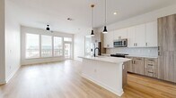 This well-appointed 2-bedroom, 2-bathroom residence offers a thoughtfully designed single-floor layout with modern finishes throughout. The open-concept kitchen and living area serves as the heart of the home, anchored by a large center island with a white quartz countertop, matte black fixtures, and stylish pendant lighting. The kitchen features two-tone cabinetry—crisp white upper cabinets paired with warm wood-toned lower cabinets—complemented by a subway tile backsplash and a full suite of stainless steel appliances. Light hardwood flooring flows seamlessly throughout the space, enhancing the bright, airy atmosphere created by large windows that invite abundant natural light and urban views. The living area provides generous, open space with a ceiling fan overhead. Each bedroom is well-proportioned, featuring hardwood floors, ceiling fans, and windows offering exterior views. The primary bedroom connects to a spacious bathroom complete with a glass-enclosed shower, soaking tub, wood-toned vanity with a white sink, and large-format tile flooring, alongside a dedicated walk-in closet with wire shelving. A second closet and an in-unit laundry room with a full-size washer round out the functional and practical offerings of this contemporary residence.