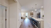 Located at Club Exchange Drive in Holly Springs, NC, this single-floor, 2-bedroom, 2-bathroom residence offers a thoughtfully designed open-concept layout. The combined kitchen and living area serves as the heart of the home, where rich hardwood-style flooring flows throughout. The modern kitchen stands out with crisp white shaker cabinets, a subway tile backsplash, stainless steel appliances, and a large granite-topped island with bar seating and pendant lighting — ideal for both cooking and casual dining. The living room is bright and welcoming, with a ceiling fan, neutral tones, and French doors that open to the outdoors. The spacious primary bedroom features plush carpeting, multiple windows for natural light, a ceiling fan, and a walk-in closet equipped with wire shelving and built-in basket organizers. The second bedroom also offers carpet flooring, a large window, and its own accent wall. Each bathroom is finished with granite vanities; one includes a frameless sliding glass walk-in shower. A dedicated laundry room with side-by-side washer and dryer hookups adds everyday convenience. A connecting hallway ties the layout together, creating a functional and cohesive living environment throughout.