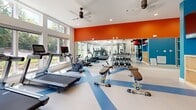 Located at 1801 Meridian St in Nashville, Tennessee, this well-appointed fitness center delivers a comprehensive workout environment designed to accommodate a wide range of exercise routines. The space is defined by its bright, open layout, with an abundance of natural light streaming in through large, floor-to-ceiling windows that offer views of lush greenery and landscaped outdoor surroundings.

The interior design features a bold and energizing color palette, with a striking orange accent wall paired with vibrant teal-blue tones and a dynamic multi-colored floor that adds visual energy to the space. Full-length mirrors along one wall amplify the sense of openness and allow for proper form monitoring during workouts.

The cardio zone is well-equipped with multiple treadmills and elliptical machines, all positioned to take advantage of the scenic outdoor views. A functional training area houses a professional-grade Hoist cable machine, along with a comprehensive free weights section featuring a full dumbbell rack, adjustable benches, and kettlebells in a range of sizes. A dedicated functional fitness station includes medicine balls, stability balls, and resistance training accessories neatly organized on a multi-tier storage rack.

Ceiling fans provide comfortable airflow throughout, and recessed lighting supplements the ample natural light. This fitness center offers a motivating, thoughtfully designed environment for a thorough and varied workout experience.