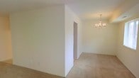 This single-floor space offers a practical and well-organized layout designed for comfortable everyday living. The main living area is generously proportioned, featuring soft carpeted flooring and crisp, neutral-painted walls that create a bright and welcoming atmosphere. An elegant chandelier serves as a focal point, adding a touch of refinement to the open space. A partial wall thoughtfully defines the transition between areas while maintaining an open, airy feel throughout.

The kitchen is neatly arranged and equipped with essential appliances, cabinetry, and counter space, making it both functional and efficient. Its placement adjacent to the main living area allows for a natural flow between cooking and entertaining spaces.

The bathroom is well-appointed, featuring a bathtub and the necessary fixtures in a clean, straightforward layout. Light-toned walls and flooring carry the cohesive neutral palette found throughout the rest of the space.

Overall, the design emphasizes simplicity and functionality, with consistent light finishes, carpeted living areas, and a logical floor plan that makes excellent use of the available space. The clean aesthetic and neutral tones provide a versatile backdrop suited to a variety of interior styles and furnishing choices.