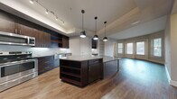This contemporary 950 square foot apartment offers a harmonious blend of style and functionality. The open-concept layout seamlessly integrates the kitchen and living area, creating a spacious feel. The kitchen boasts dark wood cabinetry, stainless steel appliances, and a large island with built-in storage, perfect for casual dining or entertaining.

Both bedrooms feature plush carpeting and ample closet space, with the primary bedroom spanning a generous 150 square feet. The bathrooms are elegantly appointed with modern fixtures, including a glass-enclosed shower in one and a tub-shower combination in the other, both showcasing sleek white tile work.

Throughout the apartment, a neutral color palette of soft greys and whites creates a calming ambiance, while large windows allow natural light to flood the space. The living areas and kitchen boast durable hardwood flooring, adding warmth and sophistication.

Attention to detail is evident in the modern light fixtures, crisp baseboards, and stylish interior doors. The apartment's thoughtful design maximizes space efficiency while maintaining a sense of openness and flow between rooms. This residence offers a perfect balance of comfort and contemporary urban living.