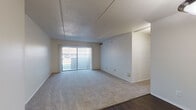This single-floor unit offers a practical and well-organized layout with distinct living, sleeping, kitchen, and bathroom areas. The living room is generously proportioned, featuring neutral-toned carpet, white walls, and a textured ceiling. A sliding glass door fitted with vertical blinds allows natural light to fill the space and provides outdoor access. The transition from carpet to dark hardwood-style flooring marks the boundary toward the kitchen and entry areas, adding visual contrast throughout.

The kitchen is equipped with stainless steel appliances, including an electric range with overhead ventilation and a dishwasher. Warm wood-toned cabinetry extends to the upper and lower sections, complemented by clean white countertops that provide ample workspace. Dark hardwood-style flooring continues through this area, contributing to a cohesive feel.

The bedrooms are carpeted and bright, each featuring vertical-blind-covered windows that admit natural light while maintaining privacy. The rooms offer clean, neutral walls well-suited for a variety of arrangements.

The bathroom is finished with dark hardwood-style flooring, a white tile tub-and-shower surround, a toilet, and a vanity with a wood cabinet base and white countertop. The overall unit presents a clean, functional environment throughout.