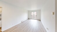 Located at 6965 Rue De Choisy in Saint-Léonard, Québec, this 1-bedroom, 1-bathroom unit offers a clean and functional layout across a single floor. Light wood laminate flooring flows consistently throughout the space, contributing to a bright and cohesive aesthetic.

The living room is an open, rectangular space with white walls and recessed lighting, creating a neutral and welcoming atmosphere. A hallway connects the main areas seamlessly, providing efficient flow throughout the unit.

The bedroom features a window overlooking a green outdoor area, allowing for natural light and garden views. A full-width sliding closet provides ample built-in storage, and a baseboard heating unit ensures year-round comfort.

The kitchen is efficiently designed with white cabinetry, dark countertops, and a classic white subway tile backsplash. Gold-toned cabinet hardware adds a subtle decorative touch, while the L-shaped layout maximizes counter and storage space.

A second room, featuring a sliding glass door opening to a private balcony, offers versatile use as a sitting area or additional living space with access to outdoor views.

The bathroom is finished with floor-to-ceiling white square tiles surrounding a full bathtub and shower combination, complemented by wood-toned flooring for a clean, classic look. The unit's overall design emphasizes simplicity, functionality, and bright, well-maintained finishes throughout.