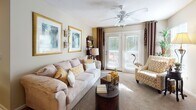 Located at 3918 St Ives Rd in Myrtle Beach, South Carolina, this single-floor residence offers a thoughtfully laid-out and comfortable living environment. The living room is a welcoming space, featuring plush carpeting, a ceiling fan, and a set of French doors flanked by large windows that allow abundant natural light and provide access to an outdoor area. The open, airy feel is enhanced by warm neutral tones throughout.

The galley-style kitchen is equipped with light wood cabinetry, ample counter space, and a full suite of white appliances including a refrigerator, electric range, built-in microwave, and dishwasher. Hardwood-style flooring runs through the kitchen, which also offers direct access to an in-unit laundry area with a full-size washer and dryer. A dedicated dining area sits just off the kitchen.

The primary bedroom is generously sized with soft carpeting, a ceiling fan, and large windows dressed with drapes that filter natural light. It includes direct access to a private en-suite bathroom and a walk-in closet with built-in shelving. A second bedroom offers similar comfort and is served by a full bathroom featuring a tub/shower combination and wood-tone vanity cabinetry. The layout and finishes throughout make this a practical and inviting Myrtle Beach residence.