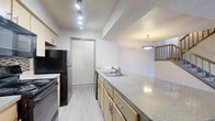 This two-story home offers a well-organized layout spread across two floors, providing comfortable living and private sleeping quarters. The main floor hosts the open-concept kitchen and living area, where a pass-through breakfast bar connects the kitchen to the living space. The kitchen is equipped with black appliances, including a range, microwave, and refrigerator, complemented by light wood cabinetry, a tile backsplash, granite-style countertops, and track lighting overhead. The living room is highlighted by a tiled fireplace flanked by built-in shelving and cabinetry, offering both function and character. Light-toned laminate flooring runs throughout the home, creating a cohesive and clean aesthetic. A staircase leads to the upper floor, where both bedrooms are located. Each bedroom features a ceiling fan with light fixture and closet access. The primary bathroom includes a single-sink vanity with a granite-style countertop and a shower-tub combination. The second bathroom mirrors a similar design. Textured ceilings are present throughout, and the home also includes two closets for additional storage. A window in one of the bedrooms allows natural light to filter in, adding brightness to the upper level.