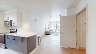 This thoughtfully designed unit at 345 Lincoln Ave in Amherst, MA offers a clean, modern aesthetic with a well-organized floor plan that maximizes every square foot. The open-concept living and kitchen area serves as the heart of the space, where light wood-tone flooring, white walls, and large windows create a bright, airy atmosphere with views of the surrounding neighborhood.

The kitchen features a galley-style layout with dark wood cabinetry on the lower level contrasted by white upper cabinets, white quartz countertops, stainless steel appliances including a dishwasher and microwave, and a matte black faucet over a single-basin sink. A peninsula with pendant lighting and bar seating connects the kitchen to the living area, enhancing the open feel.

The living room is well-lit by multiple windows fitted with horizontal blinds, offering views of the tree-lined exterior. The bedroom is a compact, functional space with light wood flooring, a window for natural light, and under-bed storage. A dedicated study nook with a window provides an ideal workspace.

The bathroom is clean and minimal, featuring a walk-in shower, light wood-tone flooring, and white walls throughout.