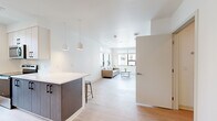 This thoughtfully designed unit at 345 Lincoln Ave in Amherst, MA offers a clean, modern aesthetic with a well-organized floor plan that maximizes every square foot. The open-concept living and kitchen area serves as the heart of the space, where light wood-tone flooring, white walls, and large windows create a bright, airy atmosphere with views of the surrounding neighborhood.

The kitchen features a galley-style layout with dark wood cabinetry on the lower level contrasted by white upper cabinets, white quartz countertops, stainless steel appliances including a dishwasher and microwave, and a matte black faucet over a single-basin sink. A peninsula with pendant lighting and bar seating connects the kitchen to the living area, enhancing the open feel.

The living room is well-lit by multiple windows fitted with horizontal blinds, offering views of the tree-lined exterior. The bedroom is a compact, functional space with light wood flooring, a window for natural light, and under-bed storage. A dedicated study nook with a window provides an ideal workspace.

The bathroom is clean and minimal, featuring a walk-in shower, light wood-tone flooring, and white walls throughout.