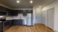 Located at 1700 W Frankford Rd in Carrollton, Texas, this single-floor residence offers a thoughtfully designed open-concept layout with contemporary finishes throughout. The living area is anchored by warm wood-style flooring, recessed lighting, and a ceiling fan, while large windows invite abundant natural light and outdoor views, creating a bright and airy atmosphere.

The kitchen is well-appointed with dark espresso cabinetry, a white tile backsplash, light countertops, and a full suite of stainless steel appliances including a refrigerator, range, microwave, and dishwasher. A double-door closet and convenient entry access are also found nearby.

The bedrooms feature plush wall-to-wall carpeting, ceiling fans, and generously sized windows fitted with blinds that allow for adjustable light and privacy. The bathrooms are finished with sleek dark vanity cabinetry, white countertops, large mirrors, and wood-style flooring. One bathroom includes a soaking tub with tile surround, while another offers a glass-enclosed walk-in shower, providing functional options for residents.

Overall, the space presents a clean, modern aesthetic with a neutral color palette, consistent quality finishes, and a practical layout suited for comfortable everyday living in the Carrollton area.
