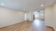 This single-floor space has been carefully updated with a clean, modern aesthetic that flows seamlessly from room to room. Light hardwood-style flooring runs throughout, creating a cohesive and airy feel across the entire layout.

The kitchen is a standout feature, showcasing gray shaker-style cabinetry with matte black hardware, crisp white countertops, and a hexagonal tile backsplash that adds a contemporary touch. Open natural wood shelving with black iron brackets provides functional display space, while stainless steel appliances — including a refrigerator, range, and dishwasher — complete the well-equipped cooking area. A single-basin stainless steel sink with a brushed nickel faucet anchors the counter space.

The kitchen opens into a bright, open living area bathed in natural light from multiple windows fitted with white blinds. A classic paneled front door with a glass insert adds charm to the entry. Recessed lighting and a textured ceiling lend character to the living space, which connects to additional rooms via open doorways.

The bedroom offers a comfortable, sunlit retreat with dual windows overlooking the surrounding neighborhood and a sleek ceiling fan for year-round comfort. Neutral wall tones and clean trim work throughout give the entire space a fresh, move-in-ready appeal.