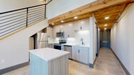 Located at 250 S Depot St in Pendleton, SC, this two-floor loft masterfully blends industrial heritage with contemporary design. The main level opens to a striking living and kitchen area with polished concrete floors, soaring ceilings, and exposed original brick walls. Large arched, multi-pane windows flood the space with natural light while framing views of the surrounding neighborhood. Reclaimed wood ceiling beams add warmth and character throughout. The modern kitchen is outfitted with stainless steel appliances, wood-toned cabinetry, a white quartz island on casters, and a classic subway tile backsplash. A sleek metal staircase with open railings leads to the upper level, where the bedroom and additional living space are situated. Two well-appointed bathrooms serve the home — one featuring warm hardwood floors, a wood-tone vanity with a framed mirror, and a marble-tiled glass-enclosed tub and shower combo, while the other offers polished concrete floors and an elegant marble-surround frameless sliding glass shower. The overall ambiance is a refined industrial aesthetic that honors the building's original character while delivering thoroughly modern comfort and style.