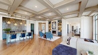 Located at 4850 Rouzan Square Ave in Baton Rouge, Louisiana, this sophisticated single-floor clubhouse at The Waverly at Rouzan offers a generously proportioned community space defined by refined architectural design and upscale finishes throughout. Gleaming hardwood floors run continuously across the open layout, while striking coffered ceilings with detailed molding lend a sense of grandeur to the main living and dining areas. The welcoming entrance features floor-to-ceiling glass doors and tall windows that flood the space with natural light. Multiple living and lounge areas offer versatile gathering spots, including a cozy room anchored by a fireplace framed with built-in shelving and cabinetry in a rich navy finish. A separate lounge area features a large built-in entertainment center with ample display shelving and decorative latticework screens for stylish division of space. The kitchen-adjacent dining area provides a large communal table beneath pendant lighting, with a full kitchen featuring stainless steel appliances, white cabinetry, and bar seating along windowed walls. A dedicated conference-style dining room with a dramatic dark ceiling, built-in cabinetry, wall-mounted display, and glass sliding doors offers a more private setting. The office area includes multiple built-in workstations with individual task lighting, ideal for focused work.