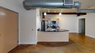 Located at 214 N Dunlop St in Petersburg, VA, this loft-style unit blends industrial character with modern conveniences. The open-plan living area immediately impresses with its polished concrete floors, exposed ductwork running across the ceiling, and a ceiling fan overhead. A striking exposed brick wall with arched windows floods the space with natural light, reinforcing the building's historic industrial heritage.

The kitchen is thoughtfully designed with light wood cabinetry, dark granite countertops, and stainless steel appliances including a refrigerator, electric range, and microwave. A curved kitchen island with a built-in sink serves as a natural divider between the living area and cooking space, making it ideal for both everyday living and entertaining.

The bedroom offers a quieter, more refined atmosphere with carpeted flooring, a tray ceiling with a contrasting dark accent, crown molding, and a generous closet. Two full bathrooms provide practical functionality; one features a glass-enclosed shower, while the other includes a tub/shower combination with sliding glass doors. Both bathrooms continue the design consistency with light wood vanities and dark granite countertops. Polished concrete flooring carries through into the bathrooms, tying the overall aesthetic together seamlessly.