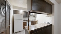 Located at 3441 Pecan Pl in Elkhart, Indiana, this single-floor residence offers a practical and straightforward layout spread across several distinct living areas. The kitchen is a notable functional space, featuring dark wood cabinetry extending to the upper walls, laminate countertops, light wood-style flooring, and white appliances including a refrigerator, electric range, and dishwasher. A peninsula with overhead cabinetry separates the kitchen from adjacent living areas, adding definition to the open layout.

The living area is generously sized and carpeted, with a standout sliding glass door fitted with vertical blinds that provides direct access to a lush green outdoor space, filling the room with natural light and outdoor views. A decorative spindle railing detail adds a subtle architectural accent where spaces transition.

The bedrooms are carpeted and well-lit, each featuring windows with blinds that allow natural light. One bedroom includes access to a walk-in closet with shelving, providing practical storage. The bathroom features light wood-style flooring, a tiled tub-shower combination, a vanity with laminate countertop, and overhead lighting. Throughout the unit, neutral wall tones and textured ceilings contribute to a clean, understated ambiance.