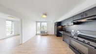 Located on the seventh floor of the Analog building in Tacoma, WA, Unit #701 is a thoughtfully designed residence that maximizes its footprint with a clean, contemporary aesthetic throughout. Light-toned hardwood-style flooring flows seamlessly across all areas, contributing to a bright and cohesive interior.

The open-concept living and kitchen area anchors the unit, with the kitchen featuring striking all-dark cabinetry, matching dark countertops, a stainless steel sink, and a full suite of black appliances including a range, refrigerator, and microwave — creating a bold, modern contrast against the white walls. A range hood adds both function and style.

The living area benefits from a large window that frames views of the surrounding Tacoma cityscape and greenery, allowing natural light to fill the space. A wall-mounted HVAC unit provides year-round climate control.

The bedroom is generously windowed, offering additional city views, and is complemented by two closets providing ample storage. A hallway connects the rooms and includes access to louvered-door storage and in-unit laundry provisions. The clean white walls and minimal design throughout give the unit a fresh, move-in-ready feel, well-suited for urban living in the heart of downtown Tacoma.
