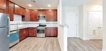 This single-floor unit is thoughtfully designed with a cohesive aesthetic that blends warm tones and modern finishes. The kitchen serves as a standout feature, showcasing rich cherry wood cabinetry with brushed nickel hardware, granite countertops with a subtle veining pattern, and a light subway tile backsplash. Stainless steel appliances, including a gas range with microwave above, complement the space. A partial wall divides the kitchen from the entry, creating a natural flow into the main living area.

The open living area is bathed in natural light through large double-hung windows that frame outdoor greenery. Light gray hardwood-style flooring runs consistently throughout the space, lending a clean, airy feel to each room. Recessed lighting and neutral warm-beige walls contribute to a bright, inviting atmosphere.

The bedrooms are generously sized, each benefiting from large windows that invite natural light and outdoor views. One bedroom connects to a spacious walk-in closet featuring built-in shelving and dual hanging rods on light hardwood floors.

The bathroom is finished with marble-look wall tile extending to mid-height, a cherry wood vanity with granite countertop, an undermount sink, and a framed mirror above — delivering a polished, upscale look.