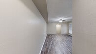 Located at Castle Gardens Drive in Arlington, TX, this one-bedroom, two-bathroom unit offers a well-organized single-floor layout designed for comfortable everyday living. Throughout the space, wood-look plank flooring in warm gray tones provides a cohesive and modern aesthetic, complemented by neutral beige walls and textured ceilings with ceiling fans in the main living areas and bedroom.

The open living room is bright and inviting, featuring built-in wall shelving, two windows with blinds that allow natural light to fill the room, and a ceiling fan for year-round comfort. The kitchen is laid out in a galley style with dark espresso cabinetry, granite-style countertops, a mosaic tile backsplash, and white appliances including a range and refrigerator. A peninsula with a paneled base and matching countertop connects the kitchen to the living area, creating a functional pass-through space.

The bedroom is a comfortable size with a window for natural light and direct access to a dedicated closet. Both bathrooms are well-appointed; one features a full soaking tub with a marble-look tiled surround, dark cabinetry, and light countertops. The overall design is clean and practical, making this a functional and attractive space in the heart of Arlington.