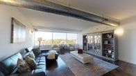 Located at 951 Government St in Mobile, Alabama, this single-floor urban residence delivers a striking industrial-modern aesthetic throughout. Polished concrete floors run seamlessly across every room, while exposed metal ductwork overhead adds a bold, loft-inspired character to the living spaces.

The expansive living area is anchored by floor-to-ceiling windows that flood the room with natural light and frame panoramic views of the surrounding cityscape and treetops. A set of elegant glass-panel sliding barn doors adds a sophisticated architectural detail to the space.

The kitchen is outfitted with contemporary flat-front cabinetry, a dark tile backsplash, stainless steel appliances, and a mobile island with bar seating — combining style and functionality. Wide windows throughout the secondary spaces continue to offer impressive elevated views of downtown Mobile's skyline.

The spacious primary bedroom features a continuous band of windows along one wall, bathing the room in abundant natural light while showcasing far-reaching outdoor views. Both bathrooms are appointed with tiled walk-in showers with glass enclosures and share the same polished concrete flooring found throughout the unit.

Overall, this residence offers a cohesive urban-industrial design with refined finishes, generous natural light, and commanding views of Mobile, Alabama.