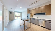 Located at Harbor Point in Stamford, CT, this two-bedroom, one-bathroom residence offers a well-planned single-floor layout designed for comfortable urban living. Light hardwood-style flooring flows consistently throughout, creating a cohesive and clean aesthetic across all rooms.

The open-concept kitchen and living area serves as the heart of the home. The kitchen is outfitted with modern flat-front cabinetry in a warm wood tone with gray lower cabinets, white quartz countertops, a classic subway tile backsplash, and a full suite of stainless steel appliances including a gas range, microwave, dishwasher, and refrigerator. Track lighting overhead enhances functionality and style. A sleek island with a gray surface provides additional prep and dining space.

The bedrooms are bright and airy, benefiting from large sliding glass doors and floor-to-ceiling windows that invite natural light and offer views of the surrounding Harbor Point neighborhood. Neutral warm-beige walls provide a calm, versatile backdrop.

The bathroom is finished with a long gray vanity featuring a white countertop, a large mirror, recessed lighting, and wood-look tile flooring. A dedicated walk-in closet with built-in wire shelving and hardwood flooring adds valuable, organized storage. Overall, the residence presents a contemporary and functional design throughout.