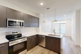 Located at 3842 W Northwest Highway in Dallas, TX, this one-bedroom, one-bathroom unit offers a well-designed layout with modern finishes throughout. Light wood-look flooring flows seamlessly across the entire space, lending warmth and continuity to each room.

The kitchen is a standout feature, outfitted with dark espresso cabinetry, white quartz countertops, and a full suite of stainless steel appliances including a French door refrigerator, electric range, built-in microwave, and dishwasher. Pendant lighting hangs above the peninsula, which also houses a stainless steel sink, creating a natural transition into the open living area beyond. Large glass doors at the end of the living space allow natural light to pour in and provide access to a private outdoor area with a grassy yard enclosed by black iron fencing.

The bedroom is a bright, comfortable retreat featuring a large window with blinds, a ceiling fan, and recessed lighting. A dedicated closet with built-in shelving provides organized storage.

The bathroom mirrors the kitchen's design language with matching dark cabinetry, a white undermount sink, and a large vanity mirror. It connects directly to the walk-in closet, enhancing the sense of a private suite. The unit also features a keypad-secured entry door for added security.
