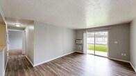 Located in Spokane Valley, Washington, this single-floor, two-bedroom, one-bathroom unit offers a practical and well-organized layout. The kitchen is a standout feature, equipped with white cabinetry, granite-look countertops, a peninsula with a built-in sink, and white appliances including a range, microwave, and refrigerator. Wood-look flooring runs throughout the kitchen and bathroom areas, adding a clean, cohesive aesthetic.

Both bedrooms are carpeted and finished with neutral gray walls, providing a calm and comfortable atmosphere. Each bedroom features a window with blinds that allows natural light to filter in, along with wall-mounted heating vents for year-round comfort. The primary bedroom includes access to a closet and an adjoining utility area. The second bedroom offers a similarly functional layout.

The full bathroom is well-appointed with a white vanity, granite-look countertop, a large mirror, and wood-look flooring that ties in with the rest of the unit. Neutral tones throughout the space create a clean, move-in ready environment. The overall design is straightforward and functional, making efficient use of the available floor area for comfortable everyday living.