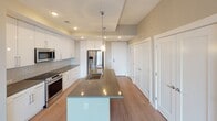Located at 6806 Morrison Blvd in Charlotte, NC, this contemporary single-floor residence showcases a clean, modern aesthetic throughout. The kitchen serves as a central highlight, featuring glossy white cabinetry extending to the ceiling, dark granite countertops, a subway tile backsplash, and a full suite of stainless steel appliances including a range, microwave, and French door refrigerator. A large central island with a granite waterfall-edge surface and integrated sink adds both function and style, illuminated by pendant lighting above. Light wood-tone flooring flows throughout the main living areas, complementing the bright, neutral color palette.

The bedrooms are carpeted for comfort and each features a ceiling fan and large windows that frame elevated views of the surrounding tree canopy and neighboring architecture, filling the rooms with abundant natural light. Two bathrooms offer a refined finish, with light wood-look tile flooring, white cabinetry, stone countertops, and backlit vanity mirrors. Each bathroom connects directly to a dedicated walk-in closet with built-in shelving, providing generous storage. The overall ambiance is modern, calm, and thoughtfully designed.