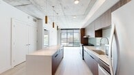 Located in the heart of Salt Lake City, this contemporary 2-bedroom, 1-bathroom residence showcases an industrial-modern aesthetic defined by striking exposed concrete ceilings, light hardwood flooring, and an abundance of natural light. The open-concept kitchen is a standout, featuring rich walnut cabinetry, a soft blue-green subway tile backsplash, stainless steel appliances, and a generously sized waterfall island illuminated by elegant brass pendant lights — ideal for both cooking and entertaining. The living area flows seamlessly toward floor-to-ceiling windows that frame urban views of the surrounding cityscape. The bedrooms are carpeted for comfort and benefit from expansive windows that flood the rooms with natural light and offer additional city views. Each bedroom is complemented by a well-organized closet with built-in shelving and hanging space. The bathroom is thoughtfully designed with light hardwood-style flooring, a warm walnut vanity with a clean white countertop, a large mirror, and a tiled walk-in shower equipped with a fold-down bench and accessibility grab bars. In-unit laundry adds everyday convenience. This residence combines urban sophistication with functional design in a prime downtown Salt Lake City location.