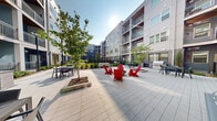 Located at 401 S Fifth St in Nashville's vibrant East Side neighborhood, this modern multi-story residential building presents a striking contemporary exterior combining brick, panel siding, and large windows across multiple levels. The architecture features a well-designed interior courtyard that serves as the centerpiece of the community, offering a generously sized open lawn area with lush artificial turf, ideal for outdoor recreation and relaxation.

Surrounding the courtyard, meticulously maintained landscaping features a variety of shrubs, ornamental grasses, mulched garden beds, and young trees that add greenery and a sense of natural serenity. Black iron perimeter fencing encloses the outdoor spaces, providing both structure and a sense of privacy. A warm wood-toned deck walkway runs along one side of the building, connecting key access points and offering elevated views into the landscaped grounds.

Ground-floor units feature private outdoor patios with artificial turf, while upper-floor residences enjoy individual balconies with metal railings overlooking the courtyard below. The building also includes pet-friendly amenities, including a dedicated pet station near the courtyard entrance. Tall street lamps illuminate the outdoor areas, enhancing the usability and ambiance of the space after dark. The overall environment conveys a clean, well-appointed, and community-oriented design.