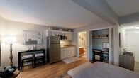 Located at 722 S Dargan St in Florence, South Carolina, this single-floor studio is thoughtfully designed to maximize functionality within an open, efficient layout. Light gray walls, a textured ceiling, and warm hardwood-style flooring flow throughout, creating a cohesive and inviting atmosphere.

The main living area combines sleeping, lounging, and dining spaces seamlessly. A built-in Murphy bed with rustic wood cabinetry and integrated shelving serves as a central design feature, allowing the space to transition easily between uses. A sofa and area rug define a comfortable sitting area, while a compact dining set provides a dedicated space for meals. Natural light enters through curtained windows and a glass-paned door, brightening the interior.

The kitchenette is well-equipped, featuring white cabinetry extending to the ceiling for added storage, a stainless steel full-size refrigerator, a microwave, and a single-basin sink. Adjacent to the main room, a bifold-door closet houses a built-in desk and shelving, offering a functional workspace.

The full bathroom includes a tub/shower combination with a curtain, a single-sink vanity with wood cabinetry, hardwood-style flooring, and accessibility-focused grab bars, making the space both practical and user-friendly.
