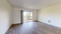 Located at 11844 26th Ave S in Burien, WA, this well-organized one-bedroom, one-bathroom unit offers a practical and comfortable single-floor layout. The open-plan living, dining, and kitchen area serves as the heart of the home, with rich hardwood-style flooring flowing throughout. The living room is bright and airy, highlighted by a sliding glass door that opens to a private balcony with leafy outdoor views, filling the space with natural light. The galley-style kitchen is efficiently designed with ample white cabinetry on both sides, a full suite of white appliances including an electric range and refrigerator, and a double sink with generous counter space. A window above the dining area brings in additional natural light and views of the surrounding greenery. The spacious bedroom features soft carpeting, two large windows that invite abundant natural light, a built-in closet, and baseboard heating. The full bathroom is clean and functional, complete with a tiled tub-shower combo, a vanity with storage, and hardwood-style flooring. Throughout the unit, four closets provide exceptional storage. A connecting hallway ties the rooms together, creating a cohesive and easy-to-navigate floor plan.