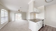 This single-story, 2-bedroom, 1-bathroom home offers a thoughtfully designed layout with a bright, open feel throughout. The combined kitchen and living area serves as the heart of the home, featuring white cabinetry, dark countertops, stainless steel appliances — including a refrigerator, range, and microwave — and a peninsula with an undermount sink. The living area is finished with plush carpeting, crown molding, a ceiling fan, and sliding glass doors that open to a private balcony, filling the space with natural light and outdoor views. A dedicated hallway connects the main living area to the bedrooms, bathroom, and laundry room. The primary bedroom is generously sized, highlighted by an arched window with crown molding detailing, a ceiling fan, and access to a walk-in closet. The second bedroom also features a ceiling fan and a large window with ample natural light. The full bathroom is finished with wood-look flooring, white cabinetry with dark countertops, and a tiled shower-tub combination. A dedicated in-unit laundry area provides added convenience. Throughout the home, a neutral color palette, consistent carpeting, and clean white trim create a cohesive and inviting atmosphere.