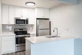 Located at 425 Park Blvd in Ogden, Utah, this two-story, one-bedroom, one-bathroom unit offers a thoughtfully designed layout that maximizes every inch of its compact footprint. The main level houses an open-concept kitchen and living area finished with light wood-look luxury vinyl plank flooring throughout. The kitchen is a standout feature, showcasing crisp white shaker cabinetry extending to the ceiling, a classic gray subway tile backsplash, light quartz countertops, and a peninsula with a built-in sink—ideal for both meal prep and casual dining. Stainless steel appliances, including a range, over-the-range microwave, and refrigerator, complete the modern culinary space. The bathroom is clean and functional, featuring a soaking tub with tiled surround, wood-look flooring, and a simple, neutral palette. Upstairs, the bedroom is a private retreat with vaulted ceilings that lend a sense of openness, a window that invites natural light, and a closet with built-in shelving. Soft carpet underfoot adds warmth and comfort to the sleeping space. Throughout, the unit maintains a cohesive, contemporary aesthetic with neutral tones and clean lines, creating a bright and welcoming atmosphere.
