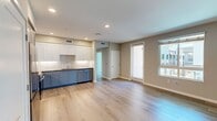 North Grove A1D is a well-appointed one-bedroom, one-bathroom apartment located in Riverside, CA, encompassing 730 square feet of modern living space. The open-concept kitchen and living area features light hardwood-style flooring, recessed lighting, and a clean, neutral color palette. The kitchen is equipped with full stainless steel appliances — including a refrigerator, range, microwave, and dishwasher — complemented by two-tone cabinetry with white upper and gray lower cabinets, a subway tile backsplash, and dark countertops. The 120-square-foot primary bedroom is finished with plush carpeting and large windows that invite abundant natural light and views of the surrounding community. A spacious walk-in closet with wire shelving and hanging rods provides generous storage. The full bathroom includes a single-sink vanity with blue cabinetry, a large mirror, and a shower-tub combination. A private balcony offers open views of the North Grove community and sunny California skies. The unit is part of a modern multi-story residential complex with clean stucco exteriors and a well-maintained courtyard setting.