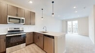Located at District Park in Mason, Ohio, this well-appointed one-bedroom, one-bathroom residence offers a thoughtfully designed open-concept layout across a single floor. The combined kitchen and living area serves as the heart of the home, featuring light wood-look flooring that creates a warm, contemporary feel. The kitchen is equipped with stainless steel appliances—including a refrigerator, range, microwave, and dishwasher—complemented by warm wood-toned cabinetry, white quartz countertops, a peninsula with an undermount sink, and stylish pendant lighting overhead. The living area flows seamlessly from the kitchen and opens to a private patio through a sliding glass door, bringing in natural light and outdoor views. The generously sized primary bedroom is finished with plush carpeting, a ceiling fan, and dual windows that allow ample natural light. Two closets provide convenient storage throughout the unit. The bathroom features a modern floating-style vanity with a white countertop, an undermount sink, and light wood-look flooring. Clean white panel doors and neutral walls throughout lend the space a crisp, move-in-ready aesthetic well-suited to a variety of lifestyles.