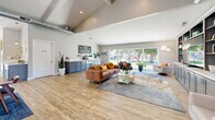 Located at 6312 Birdcage St in Citrus Heights, CA, this thoughtfully designed single-floor space offers a generous, open-concept layout that seamlessly integrates a living room and dining area. The interior is anchored by striking vaulted ceilings with exposed ductwork that lends an airy, loft-inspired character throughout. Light wood-look flooring flows consistently across the entire space, complementing the neutral, contemporary color palette.

The living area is a standout, featuring a custom built-in media wall with gray shaker-style cabinetry, open display shelving, and ample storage. Large sliding glass doors span the exterior wall, flooding the room with natural light and offering direct views of a lush green outdoor area. A dedicated coffee bar station with additional cabinetry adds a practical and inviting touch.

The dining area is framed by a full glass partition wall with sliding doors, creating a semi-private yet visually connected space. A modern pendant light fixture anchors the dining table, while French doors provide a second point of access to the outdoors. Additional seating nooks with built-in counters offer versatile, informal gathering spots. Together, these elements create a bright, welcoming, and highly functional communal environment.