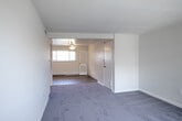 Located at 9215 Blue Grass Rd in Philadelphia, PA, this single-floor, one-bedroom, one-bathroom unit offers a functional and efficiently designed layout. The overall floor plan connects the primary living areas in a logical flow, moving from the living room through a hallway to the bedroom, with the kitchen and bathroom conveniently accessible along the way.

The living room is a generously proportioned space finished with plush gray carpeting and neutral white walls, creating a clean and versatile environment. It opens directly into the kitchen area, which features light hardwood-style flooring, dark wood cabinetry with modern hardware, a marble-style tile backsplash, and white appliances including a gas range and full-size refrigerator. A ceiling fan with a light fixture is installed overhead, and a window allows natural light to fill the combined kitchen and dining area.

The bedroom is a well-sized, carpeted room with neutral tones, a window with an exterior view, and a wall-mounted air conditioning unit. Two closets provide ample storage throughout the unit. The bathroom is finished with white subway tile wainscoting, a bathtub-shower combination, and light wood-style vinyl flooring. A hallway connects the key areas of the unit, adding to its organized and practical layout.
