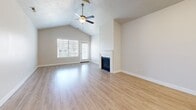 Located in American Fork, Utah, this well-appointed single-level home offers three bedrooms, two bathrooms, and a thoughtfully designed layout. The open-concept living area immediately impresses with soaring vaulted ceilings, a ceiling fan, and a sleek fireplace framed by a classic white mantel. Large windows invite abundant natural light and provide views of the surrounding neighborhood, while a private exterior door adds convenient outdoor access. Light-toned hardwood-style flooring flows throughout the main living areas, creating a cohesive, airy feel. The kitchen is a standout, featuring crisp white cabinetry, granite countertops, a center island with a sink, pendant lighting, and a full suite of stainless steel appliances. The bathrooms echo the kitchen's refined aesthetic with granite-topped white vanities and tub-shower combinations. The bedrooms are carpeted for comfort, with the primary bedroom offering generous proportions and vaulted ceiling details. Additional secondary bedrooms are bright and well-sized, each with natural light from sizable windows. A dedicated laundry room houses a full-size washer and dryer. The home's neutral color palette and consistent finishes throughout create a clean, modern ambiance well-suited to a variety of lifestyles.