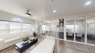 Located at 7575 Hampton Boulevard in North Lauderdale, FL, this well-appointed single-floor professional office space offers a thoughtfully designed layout that balances functionality with a refined, contemporary aesthetic. The interior is finished with warm wood-tone flooring throughout, neutral beige walls, and recessed lighting that creates a bright, welcoming atmosphere.

The space opens into a comfortable reception and lounge area, highlighted by a large picture window topped with an elegant arched transom that floods the room with natural light. A ceiling fan adds a relaxed, airy feel, while plush white seating and tasteful décor give the area a polished, professional look.

Sleek floor-to-ceiling glass partition walls with frosted privacy banding divide the space into distinct private offices or consultation rooms, offering visual transparency while maintaining a sense of separation. These glass-enclosed rooms are visible from the main area and are well-suited for meetings or private client sessions.

A dedicated workstation room features a row of built-in desk stations equipped with monitors, flanked by bold dark vertical columns and complemented by wall sconces and contemporary white task chairs — ideal for administrative or collaborative work.

Throughout the space, the design emphasizes clean lines, modern materials, and an open yet organized flow, making it a highly functional and visually impressive professional environment.