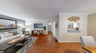This single-story, 1-bedroom, 2-bathroom home offers a thoughtfully designed layout that maximizes every square foot. Rich hardwood flooring flows throughout the main living areas, complemented by crown molding and neutral wall tones that create a warm, cohesive aesthetic. The spacious living room provides an open, airy feel, with natural light streaming in through large windows fitted with blinds. A hallway connects the living space to the private bedroom and bathrooms, maintaining a clear and functional flow. The dining area features hardwood flooring, a window with natural light, and a pass-through opening to the kitchen, adding a connected and social feel to the space. The galley-style kitchen is efficiently appointed with white cabinetry, stone-look countertops, tile flooring, and black and stainless steel appliances. The generously sized primary bedroom features plush carpeting, a ceiling fan, a dedicated closet, and a soft, calming color palette. The primary bathroom offers a wide vanity with ample cabinetry, a large mirror, and bright overhead lighting. A second bathroom provides additional convenience. A closet rounds out the home's storage options. Throughout, textured ceilings and clean finishes contribute to a comfortable, move-in-ready atmosphere.