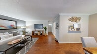 This single-story, 1-bedroom, 2-bathroom home offers a thoughtfully designed layout that maximizes every square foot. Rich hardwood flooring flows throughout the main living areas, complemented by crown molding and neutral wall tones that create a warm, cohesive aesthetic. The spacious living room provides an open, airy feel, with natural light streaming in through large windows fitted with blinds. A hallway connects the living space to the private bedroom and bathrooms, maintaining a clear and functional flow. The dining area features hardwood flooring, a window with natural light, and a pass-through opening to the kitchen, adding a connected and social feel to the space. The galley-style kitchen is efficiently appointed with white cabinetry, stone-look countertops, tile flooring, and black and stainless steel appliances. The generously sized primary bedroom features plush carpeting, a ceiling fan, a dedicated closet, and a soft, calming color palette. The primary bathroom offers a wide vanity with ample cabinetry, a large mirror, and bright overhead lighting. A second bathroom provides additional convenience. A closet rounds out the home's storage options. Throughout, textured ceilings and clean finishes contribute to a comfortable, move-in-ready atmosphere.