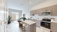 Located at 501 W Washington St in East Peoria, IL, this thoughtfully designed one-bedroom, one-bathroom unit offers a modern living experience with an efficient, well-organized layout. The open-concept kitchen and living area serves as the heart of the home, featuring taupe shaker-style cabinetry, a white quartz countertop island with bar seating, a classic subway tile backsplash, and a full suite of stainless steel appliances. Light wood-tone flooring flows throughout, complementing the neutral color palette and soaring ceilings that lend an airy, spacious feel. The living room benefits from abundant natural light through a large door with transom window, creating a bright and welcoming atmosphere. The bedroom is carpeted for comfort and includes a generous walk-in closet outfitted with multi-tier wire shelving and hanging rods. A dedicated in-unit laundry area adds everyday convenience. The full bathroom features a gray shaker vanity with a sleek rectangular mirror, and a tub-shower combination. Clean lines, elevated finishes, and a cohesive modern aesthetic are consistent throughout, making this a well-appointed and functional living space.